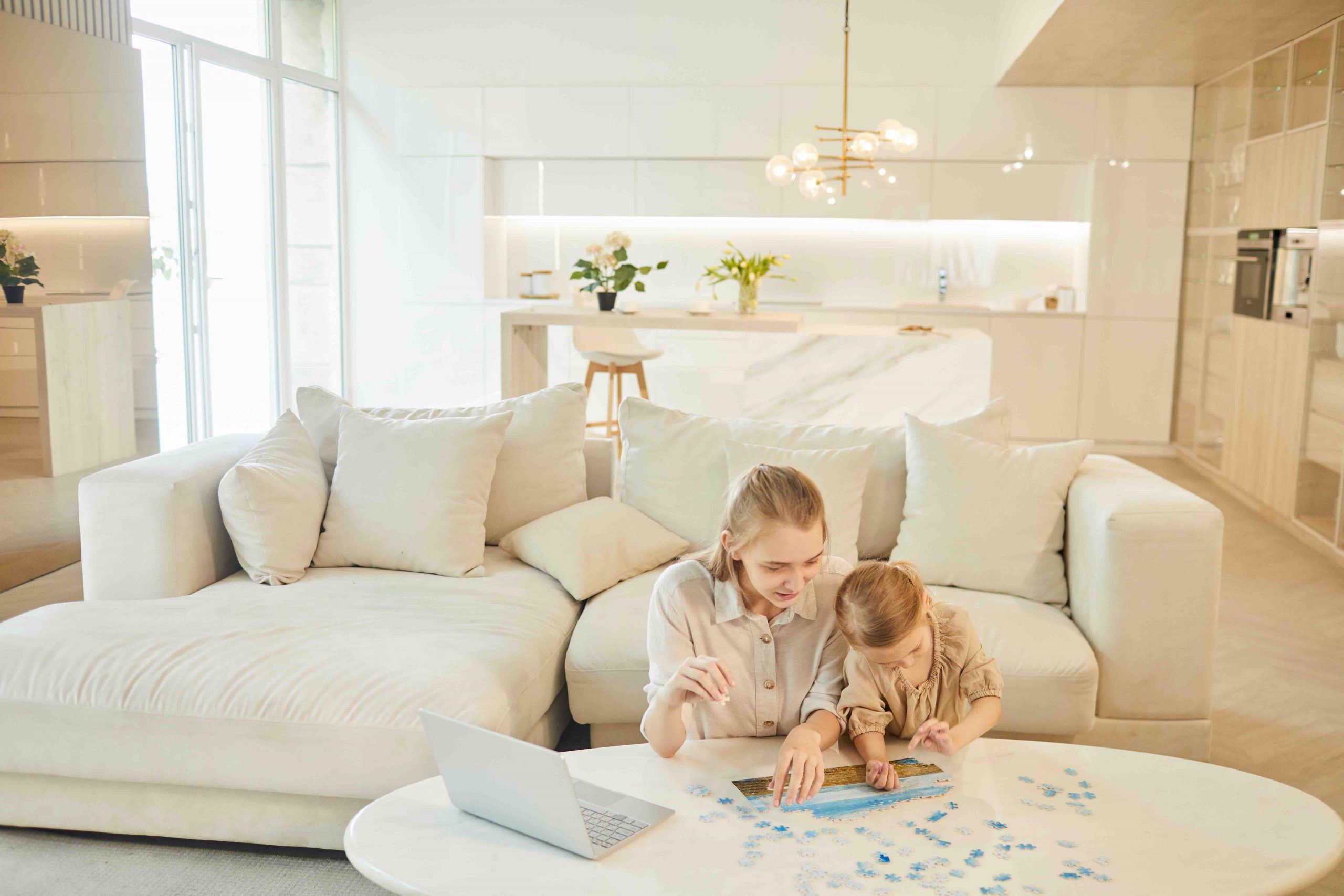 Warm-toned wide angle portrait of two sisters solving puzzle together while enjoying time at home indoors in minimal white interior, copy space